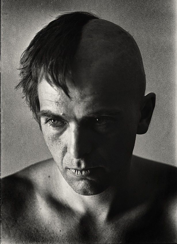 a black and white photo of a man's face with no shirt on, looking at the camera