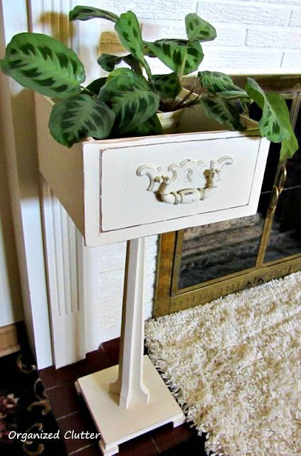 a white table with a plant in it sitting on a rug next to a fireplace