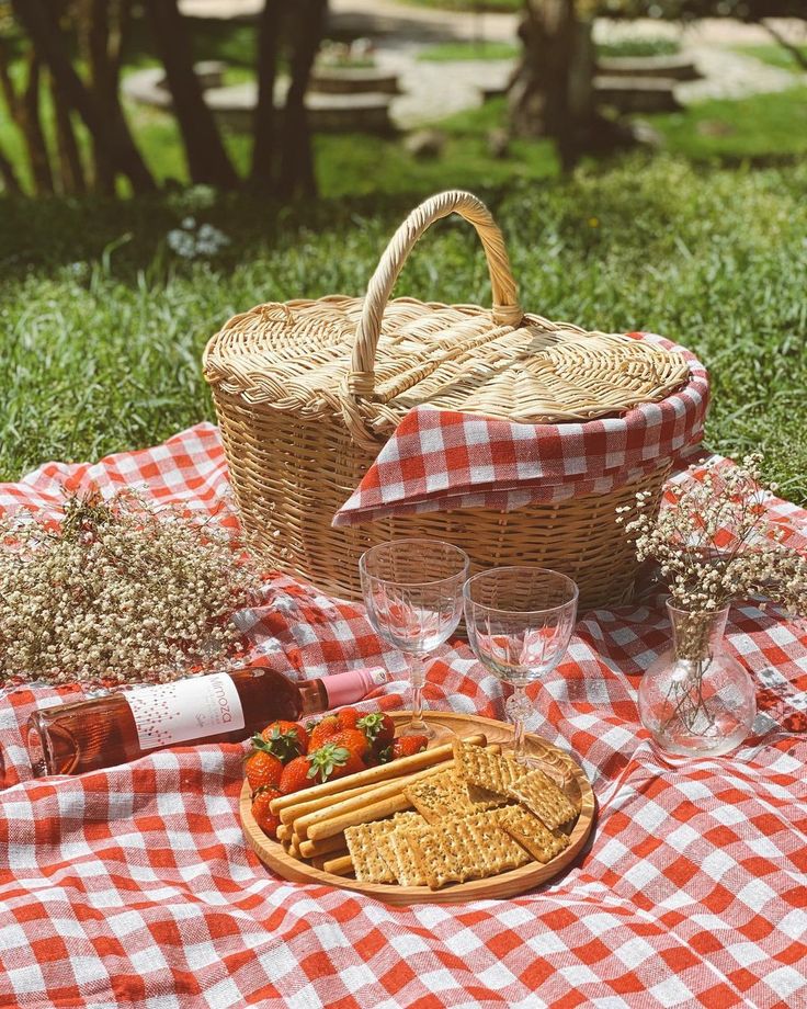 a picnic basket with crackers and strawberries on a checkered tablecloth in the grass