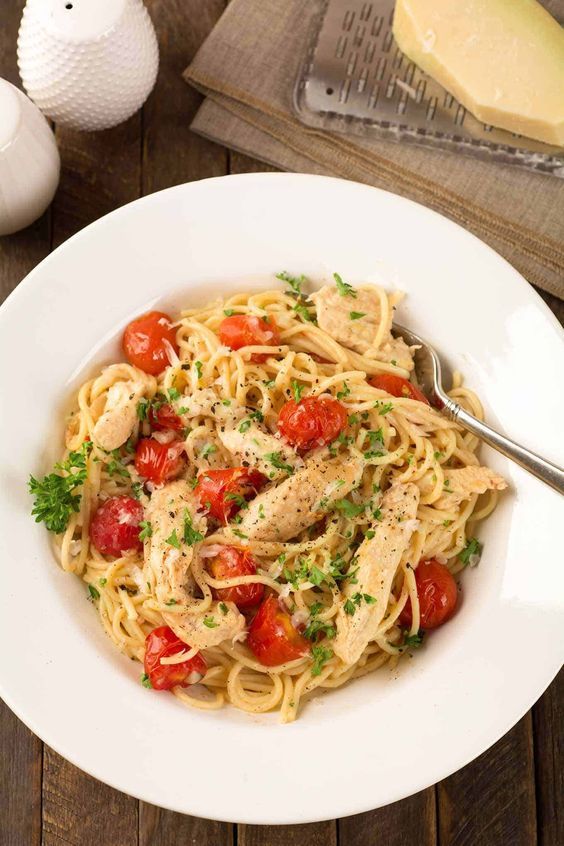 a white bowl filled with pasta topped with chicken, tomatoes and parmesan cheese