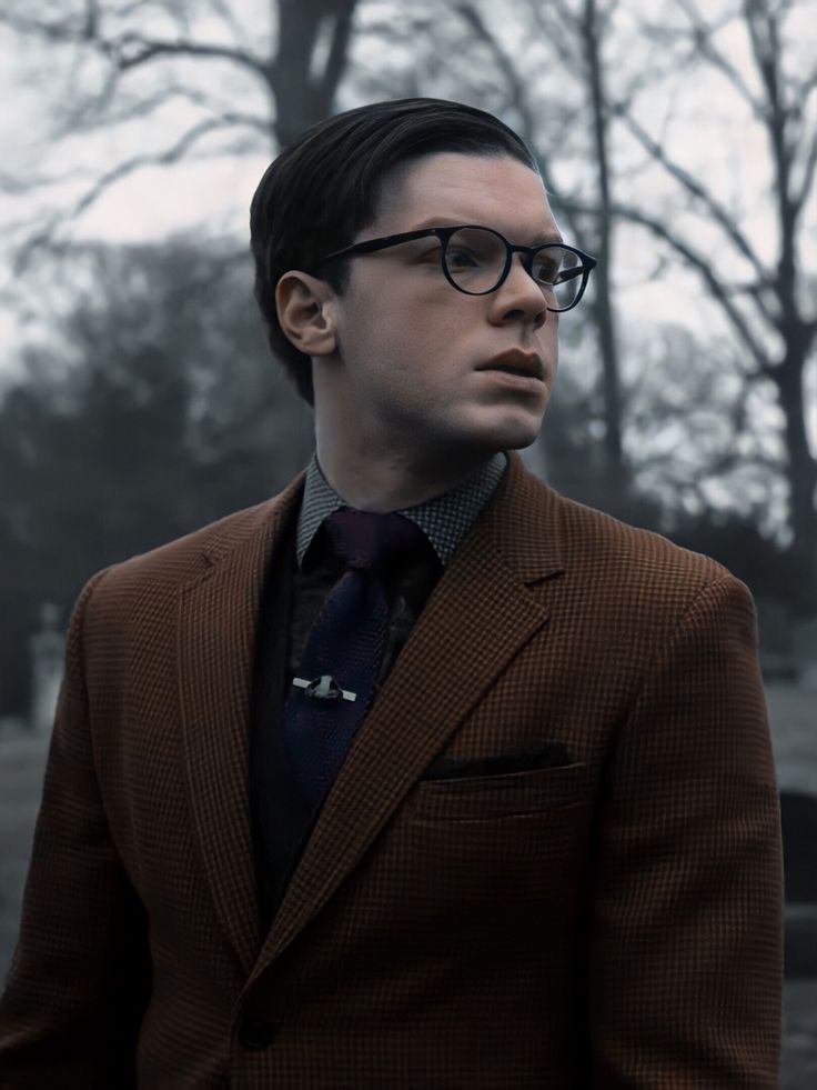 a man wearing glasses and a suit standing in front of a cemetery