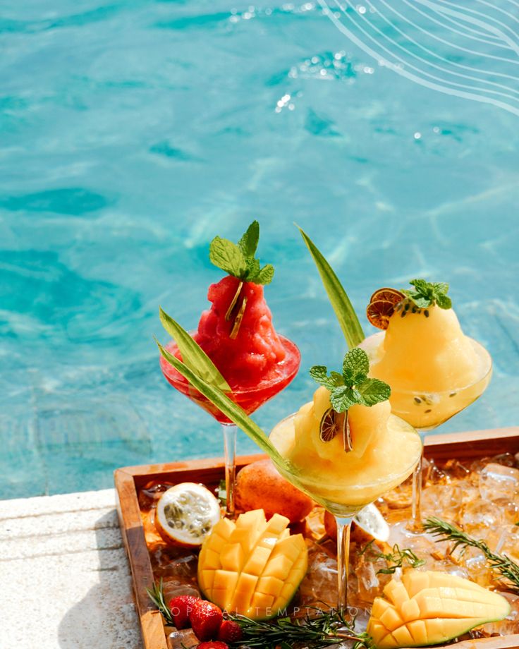 fruit cocktails are arranged on the edge of a swimming pool