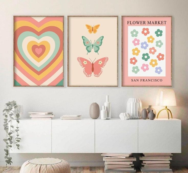 three colorful posters on the wall above a white cabinet in a living room with flowers and hearts