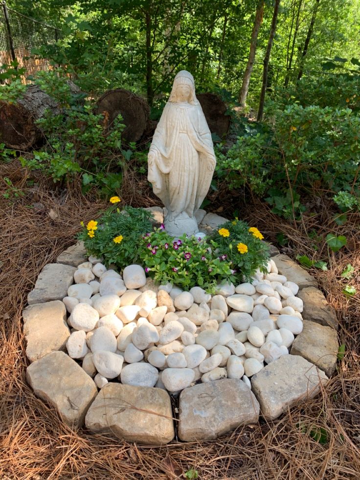 a statue is surrounded by rocks and flowers