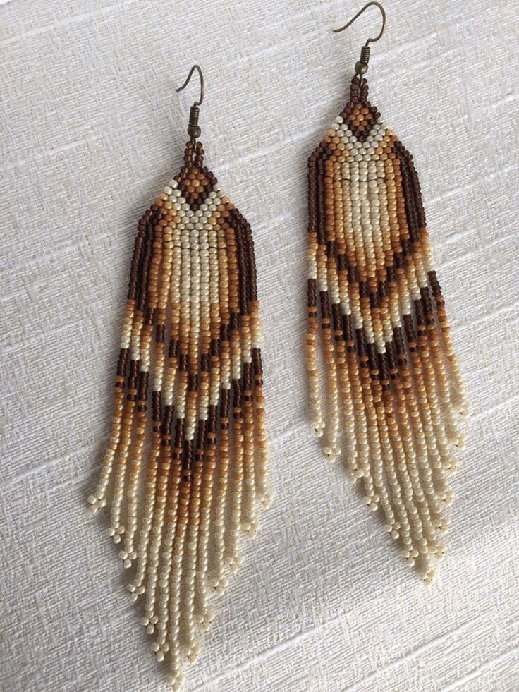 two brown and white beaded earrings on a tablecloth with a pair of scissors next to it