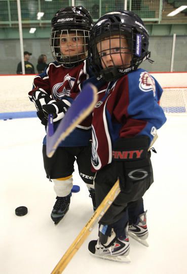 two young hockey players standing on the ice with their arms around each other and holding sticks