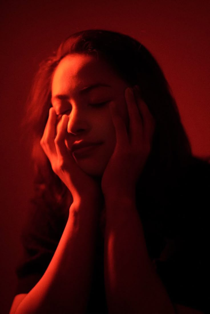 a woman is holding her hands to her face and looking down at the camera with red light behind her