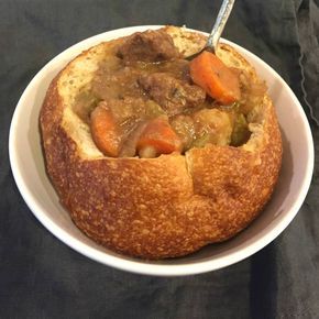 a bowl filled with meat and vegetables on top of a white plate next to a fork