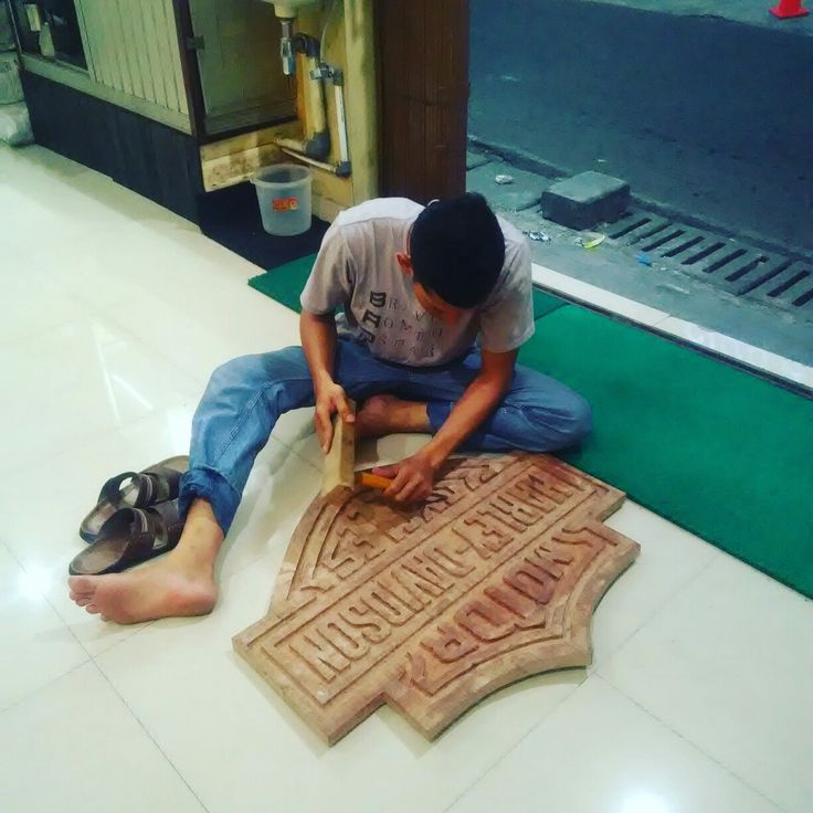 a man sitting on the ground working on a carved wooden sign with his feet propped up