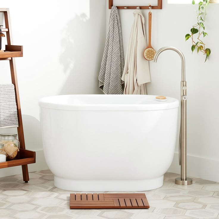 a white bath tub sitting in a bathroom next to a wooden shelf and towel rack