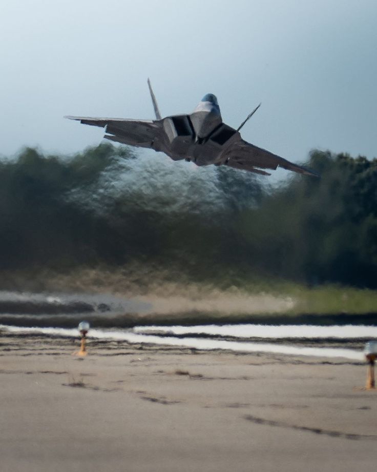 a fighter jet is flying low to the ground in front of some trees and water