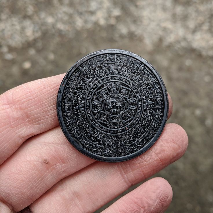 a hand holding a small black object in it's left hand, with an intricate design on the center