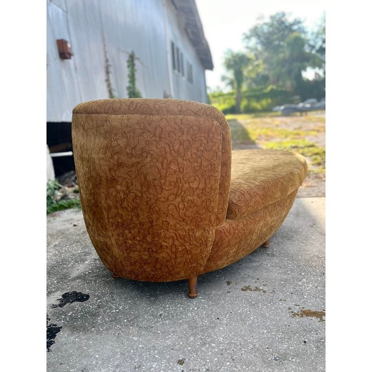 a brown chair sitting on top of cement next to a building and grass covered ground