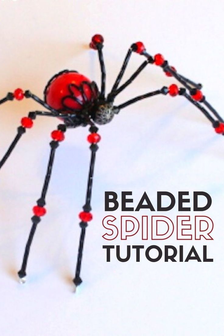 the beaded spider is made with red beads and black wire, while it sits on top of a white surface