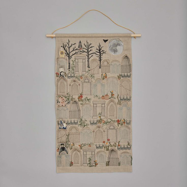 an embroidered wall hanging with birds, trees and buildings in the background on a gray wall