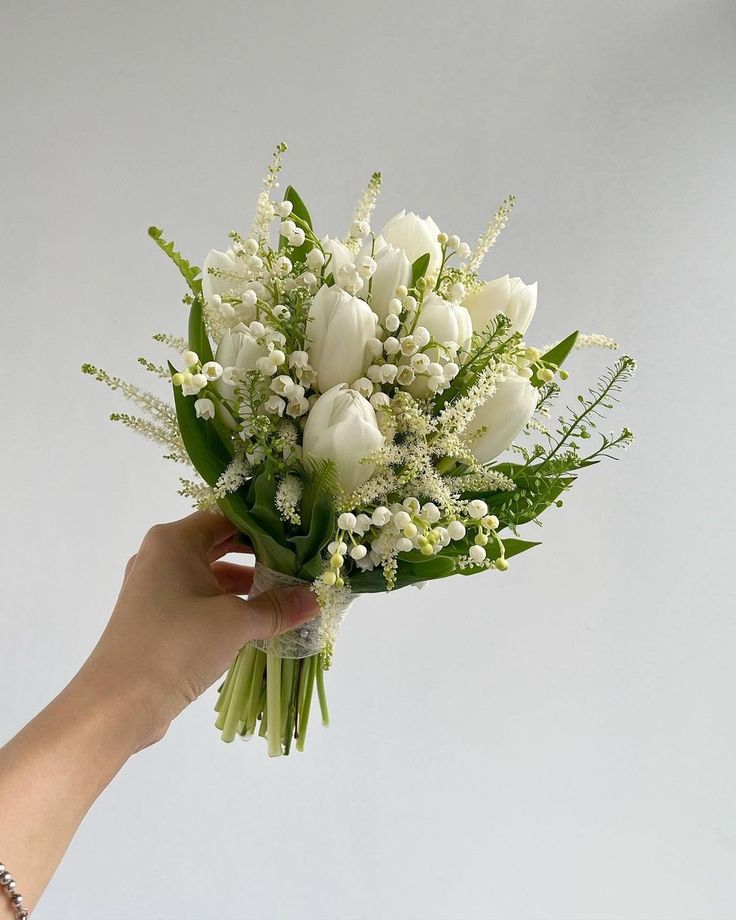 a bouquet of white tulips and baby's breath is held by a hand