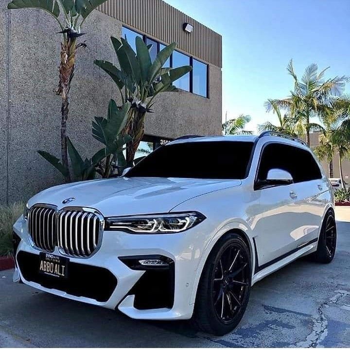 a white bmw x7 parked in front of a building with palm trees behind it