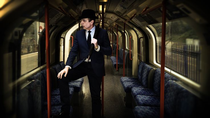 a man in a suit and top hat standing on a train with his arms out