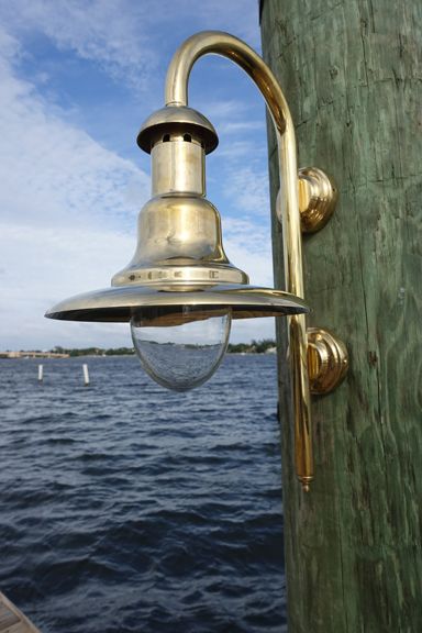 an old fashioned light on the side of a wooden post near water with boats in the background