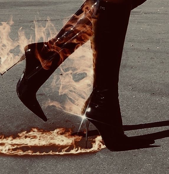 a woman's legs in high heel boots with fire painted on the ground behind them