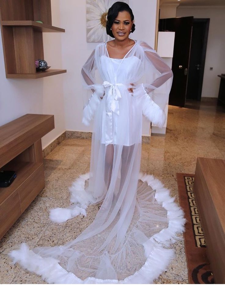 a woman in a white dress standing on a floor with feathers around her legs and wearing a veil