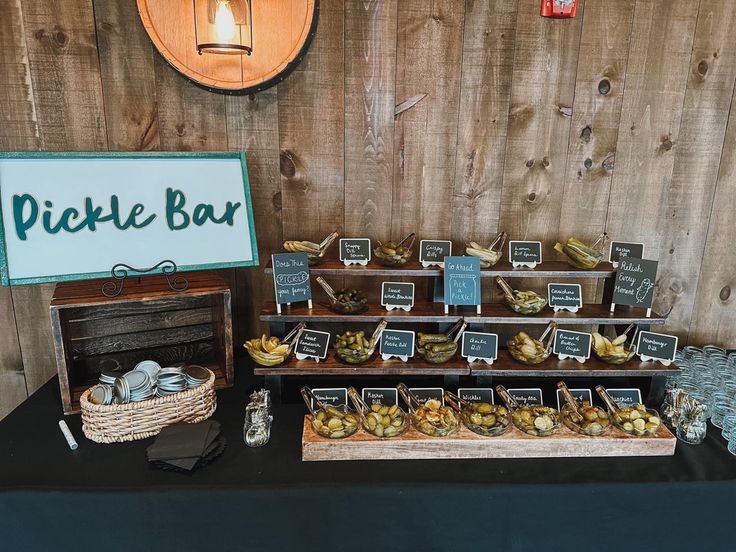 a table topped with lots of food next to a wooden sign that says pickle bar