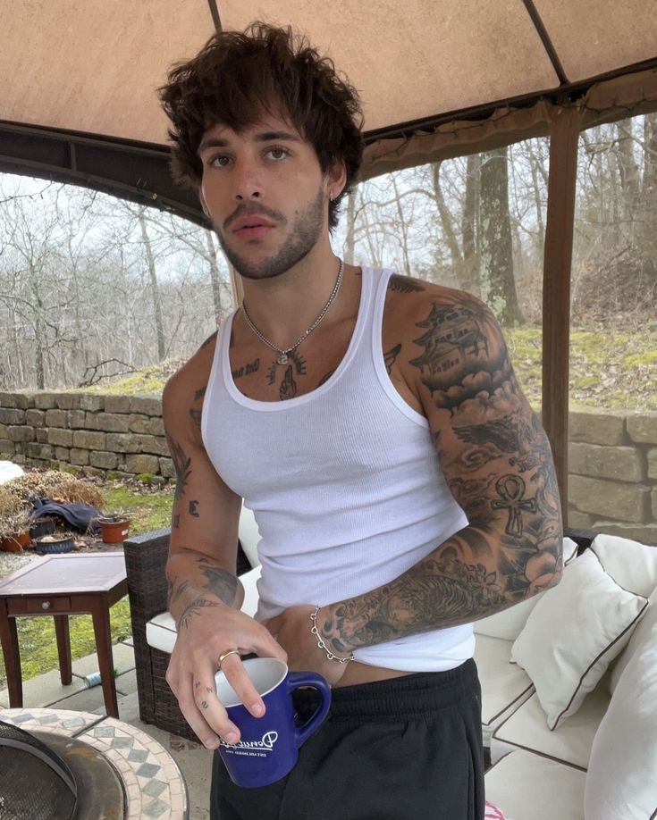 a man with tattoos on his arm holding a cup