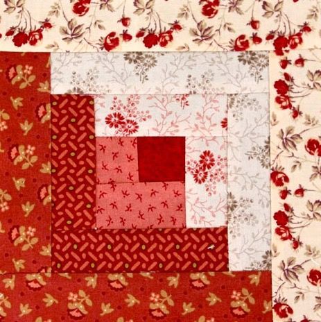 a red and white patchwork quilt with flowers on the border, in front of a flowered background