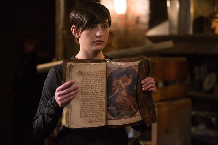 a woman is holding an old book in her hands and looking at the camera while she holds it open