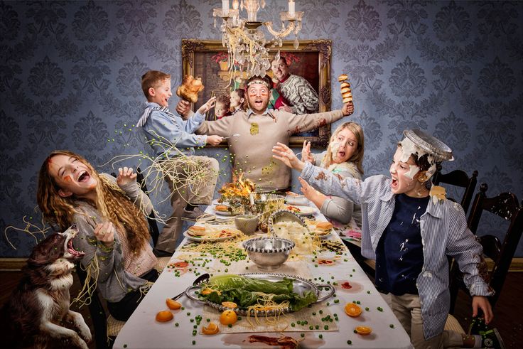 a group of people sitting around a table with food on it and one person standing in the middle