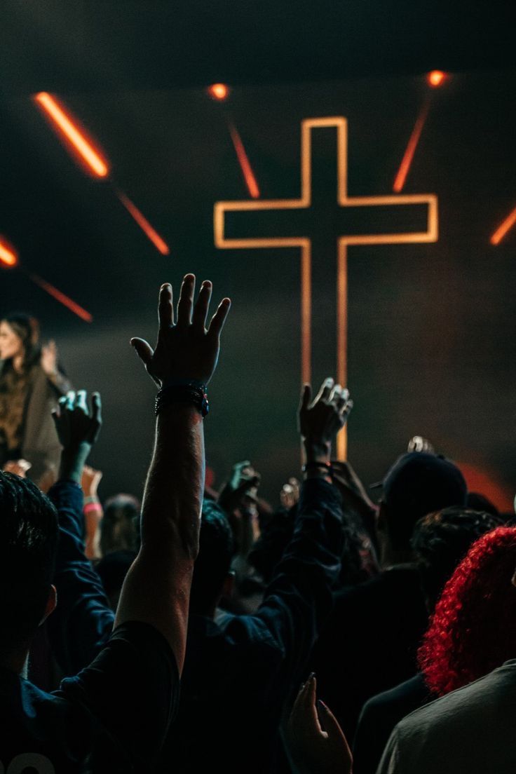 people raising their hands up in front of a cross on a stage with bright lights