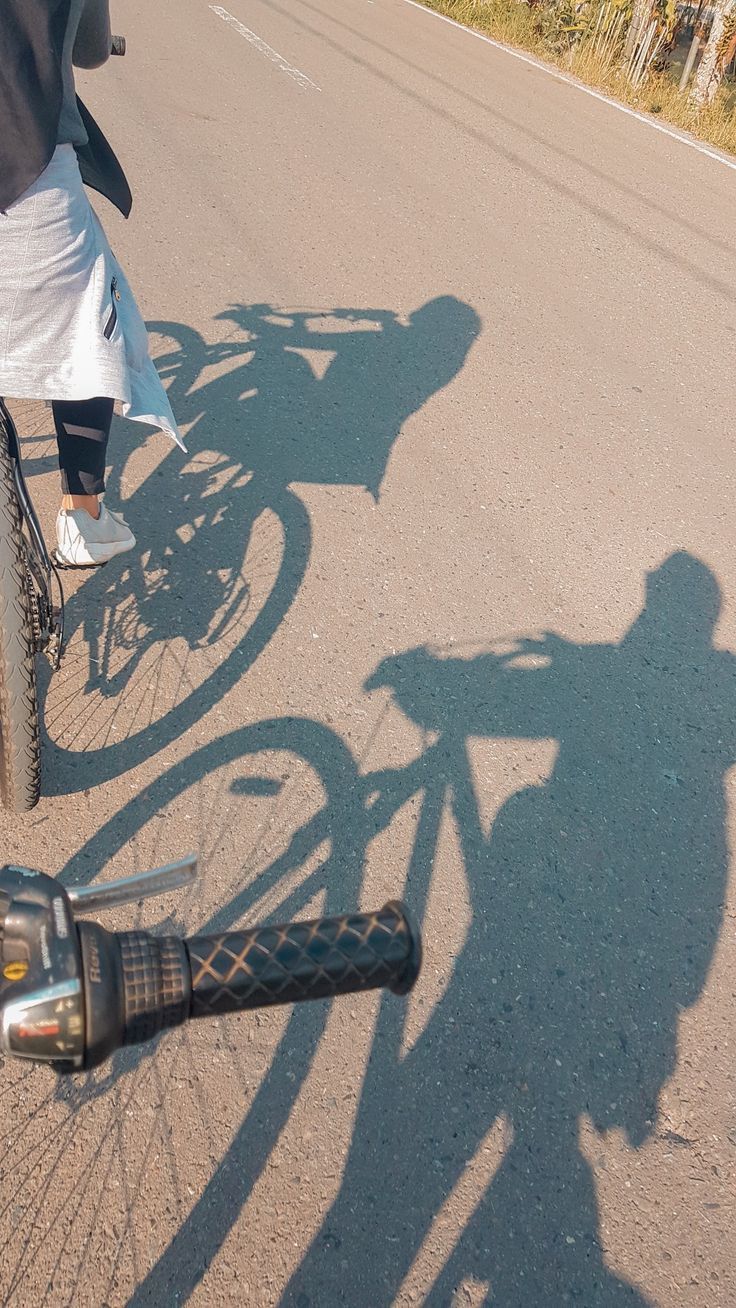 the shadow of two people riding bikes on a road next to another person's bike