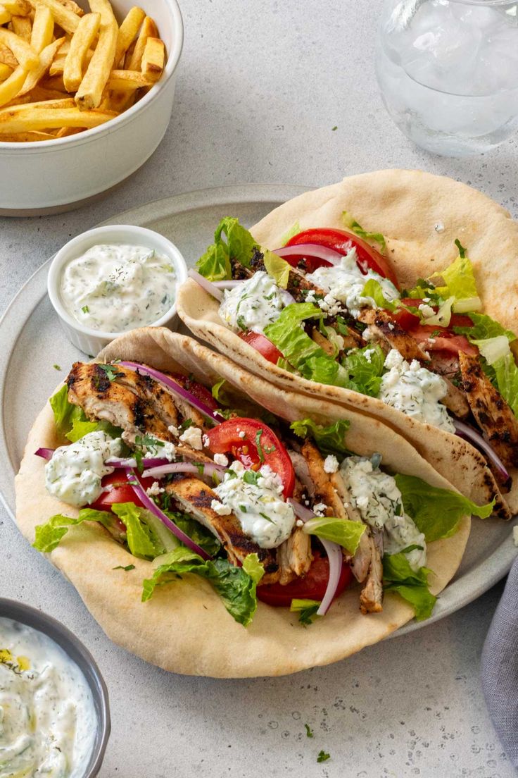 two chicken tacos with lettuce, tomatoes and onions on a plate next to french fries