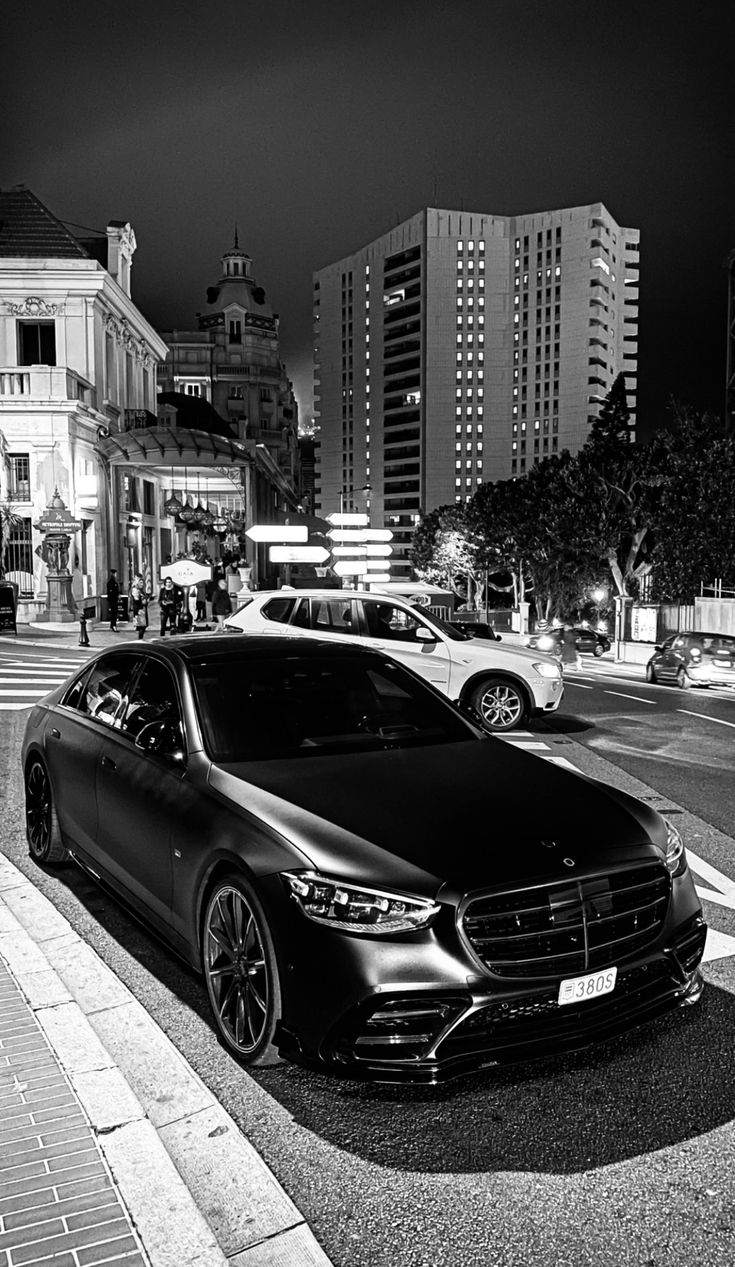 a black car parked on the side of a road next to tall buildings at night