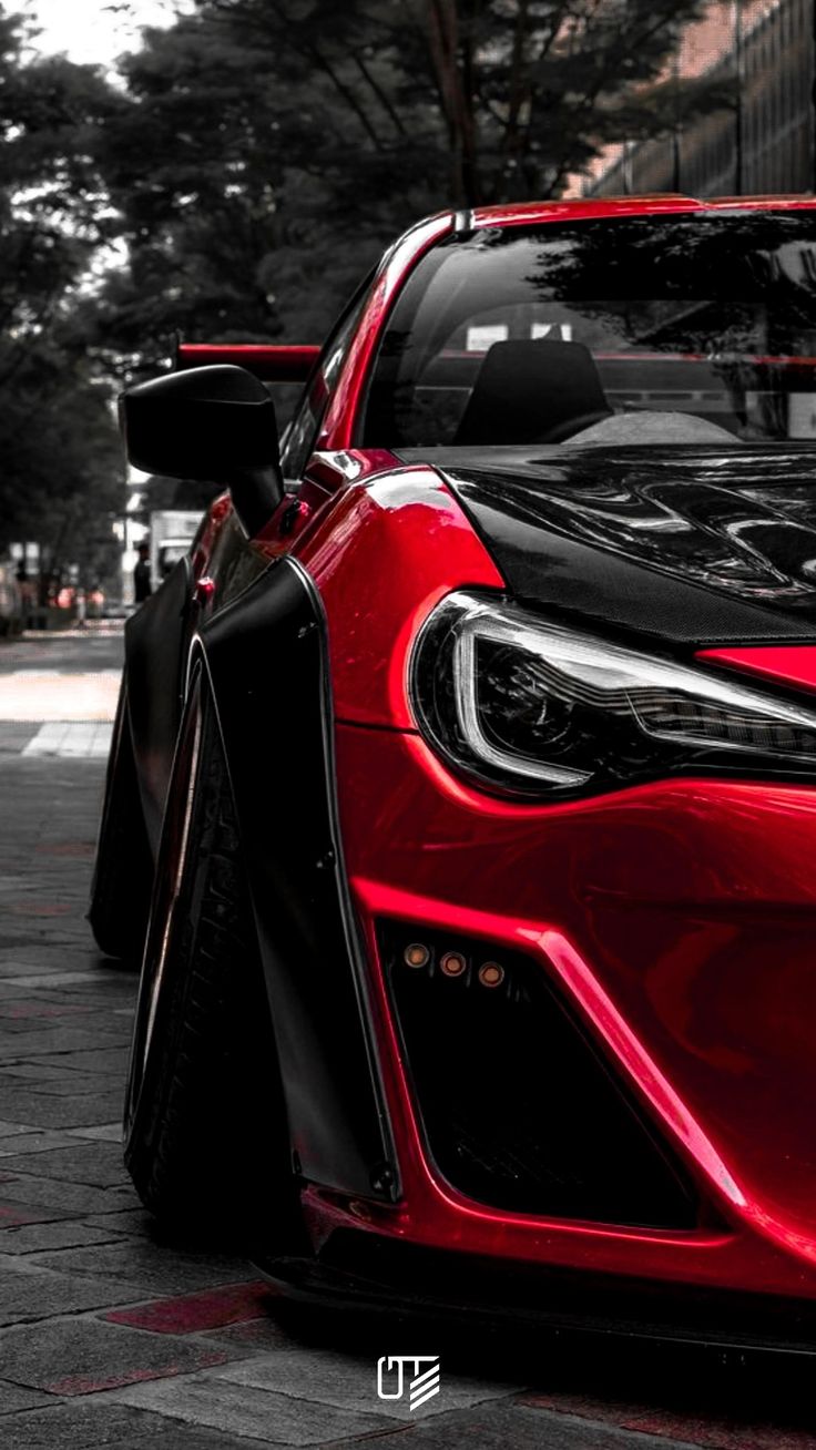 the front end of a red sports car parked on a street next to tall buildings