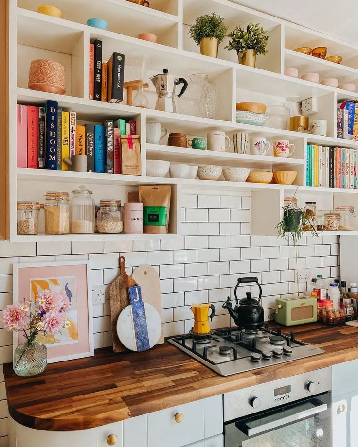 a kitchen with white cabinets and shelves filled with cookware, books, and other items