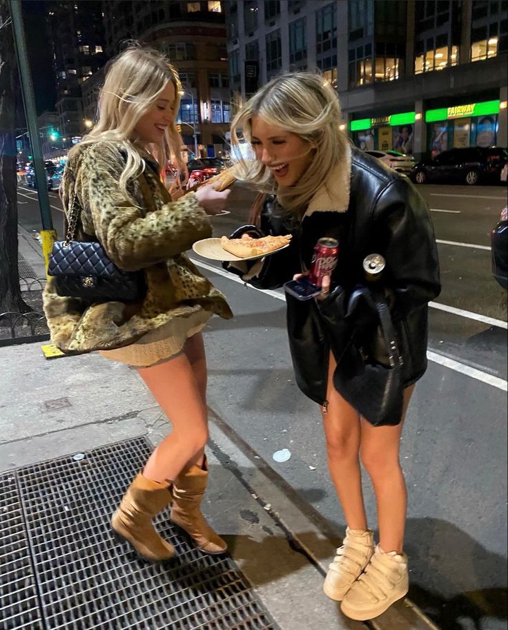 two women standing on the sidewalk eating food