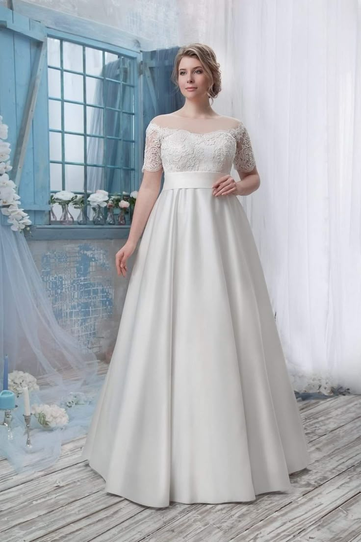 a woman standing in front of a white wall wearing a wedding dress with short sleeves