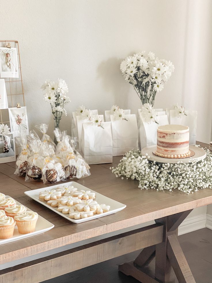 a table topped with cakes and cupcakes on top of a wooden table covered in white flowers