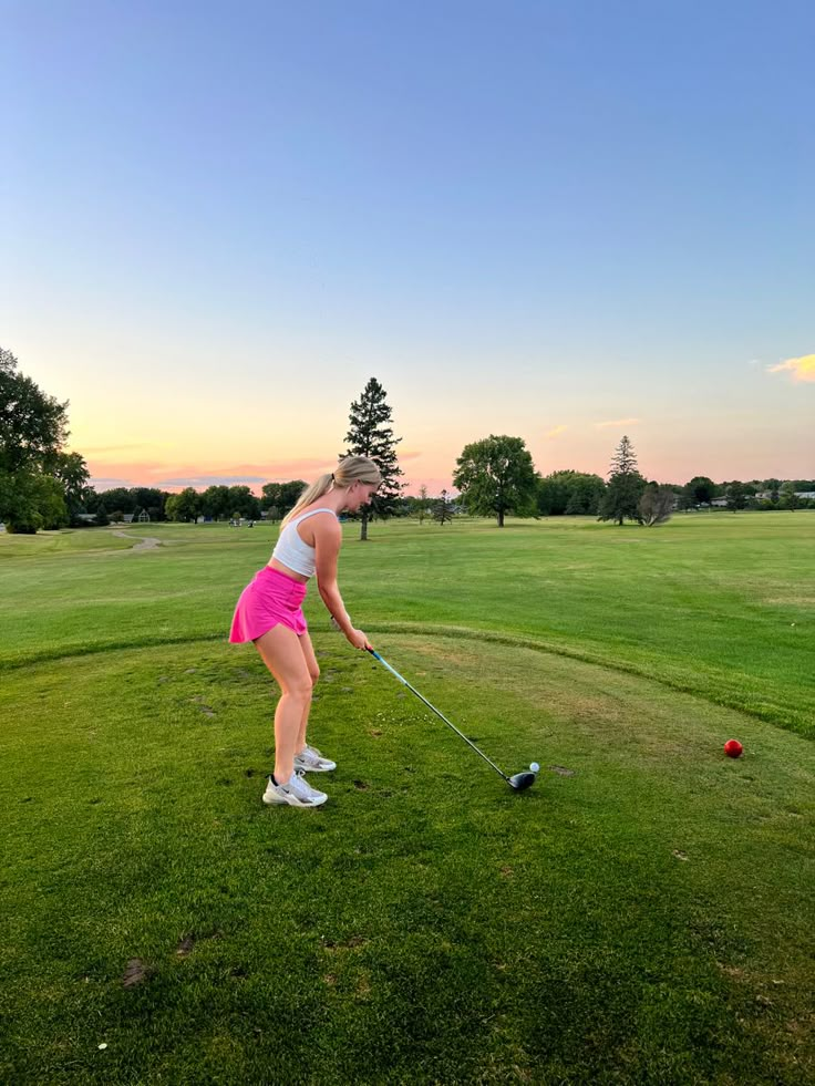 a woman in pink shorts hitting a ball with a golf club on a green field