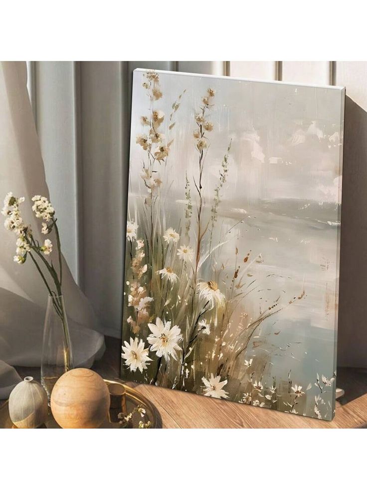 a painting on a table next to a vase with flowers in it and two other items