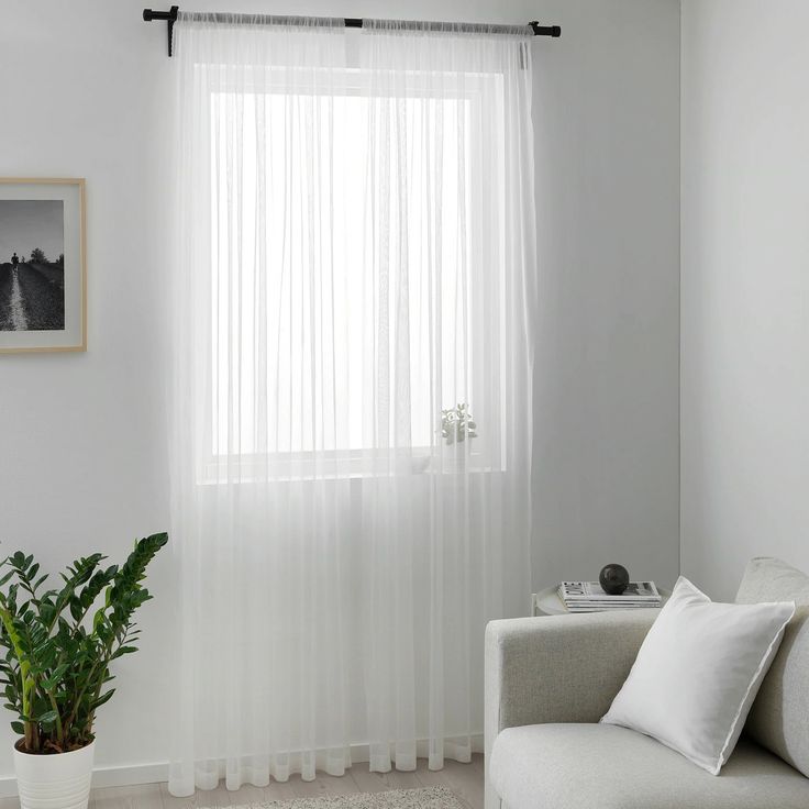 a living room with white curtains and a couch in front of a window that has a potted plant next to it