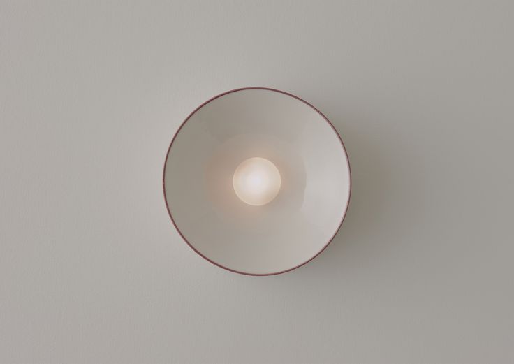 a white and red bowl with a light in the middle on a gray wall background