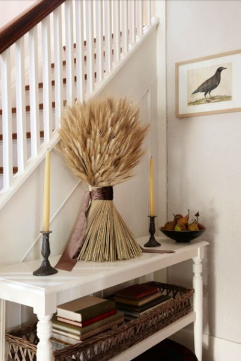 a white table topped with a vase filled with dry grass next to a stair case