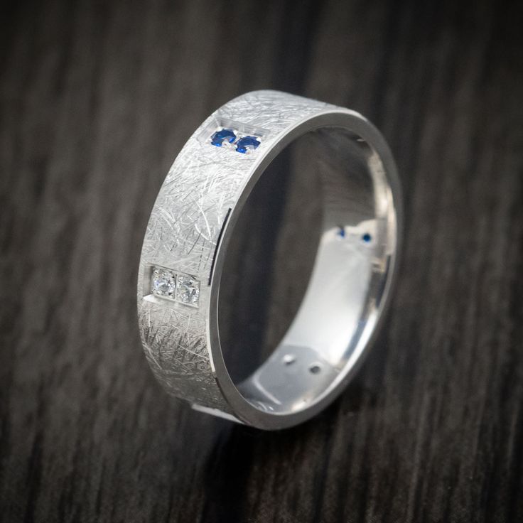 a silver ring with blue and white diamonds on it sitting on a table in front of a wooden surface