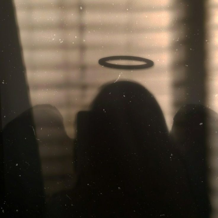 the silhouette of a person with an angel halo on their head in front of a window