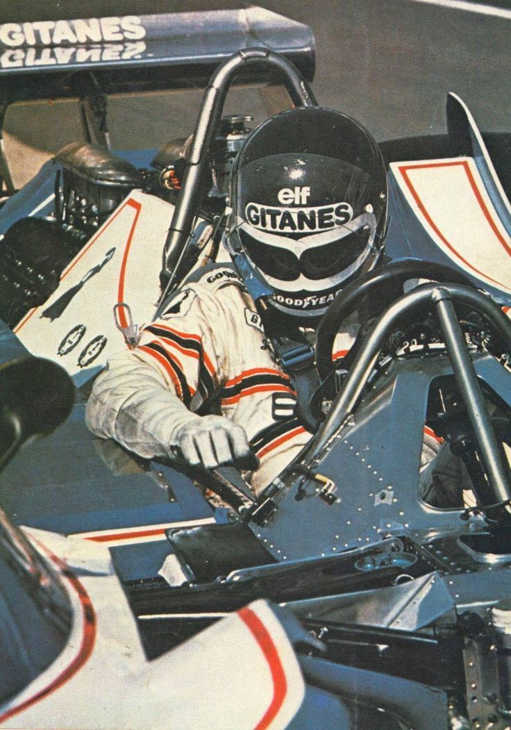 a man sitting in a racing car with his hand on the steering wheel and wearing a helmet