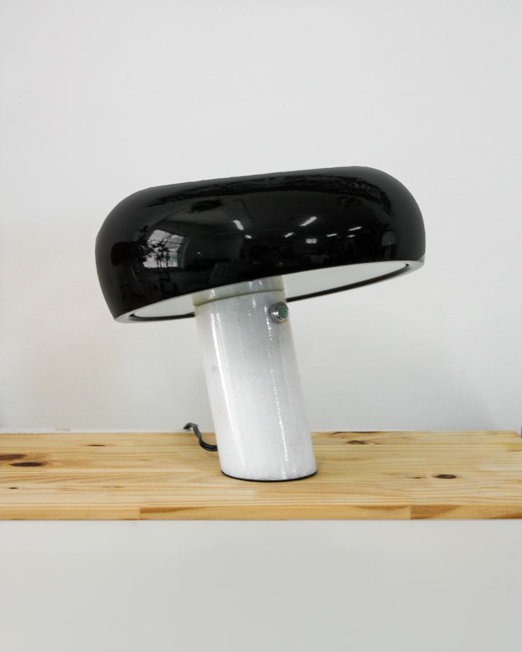 a black and white desk lamp sitting on top of a wooden shelf next to a wall