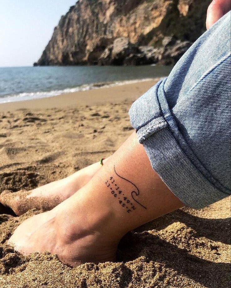 a person with a tattoo on their leg sitting in the sand