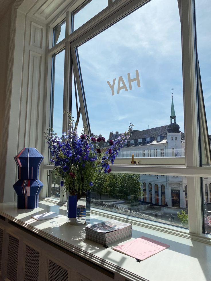 a vase with purple flowers sitting on top of a window sill next to a book